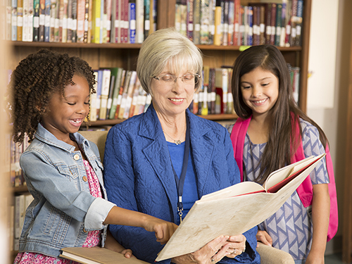 Senior woman mentoring young kids in a reading program>